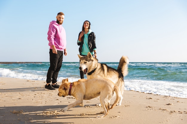 Schönes junges Paar, das mit ihrem Hund am Strand spielt