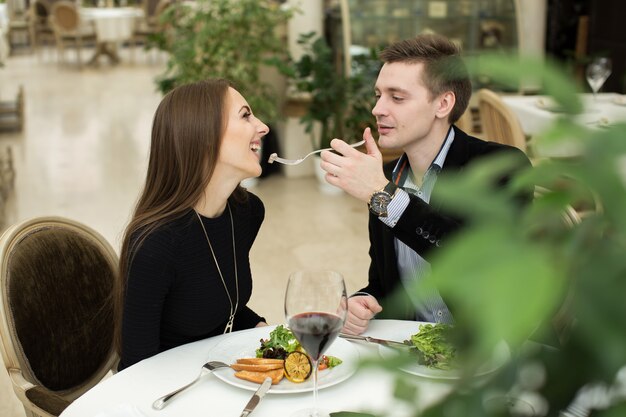 Schönes junges Paar, das sich gegenseitig füttert und lächelt, während es Zeit im Restaurant verbringt?