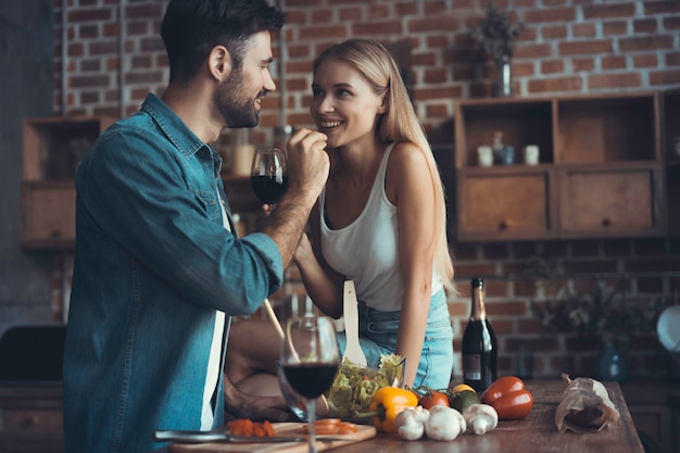 Schönes junges Paar füttert sich gegenseitig und lächelt beim Kochen in der Küche zu Hause.