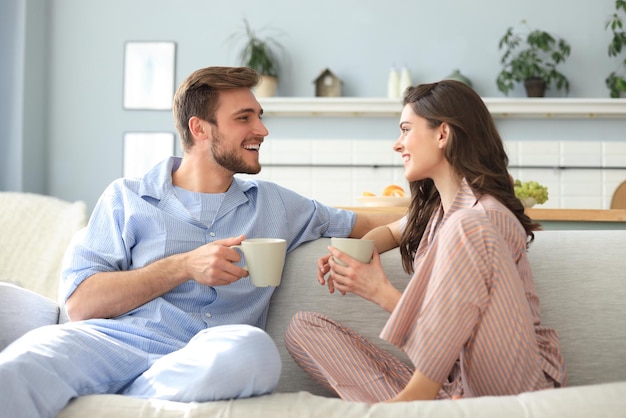 Schönes junges Paar im Schlafanzug sieht sich an und lächelt auf einem Sofa im Wohnzimmer.