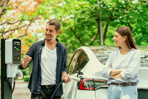 Schönes junges Paar laden im Herbst die Batterie für ein Elektroauto auf