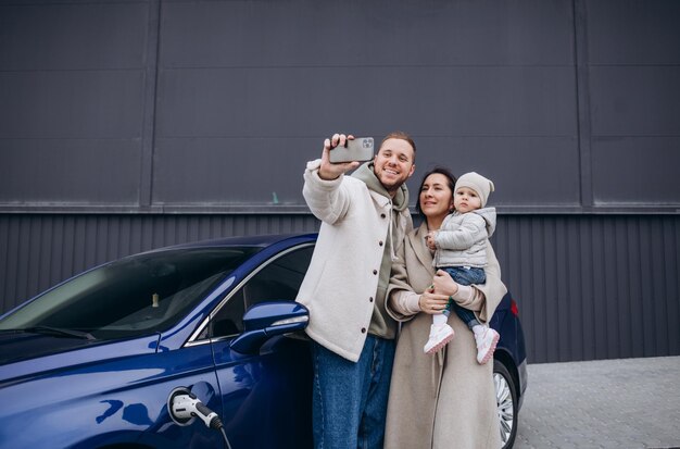 Schönes junges Paar lädt ein Elektroauto auf und macht ein Selfie auf einem Smartphone