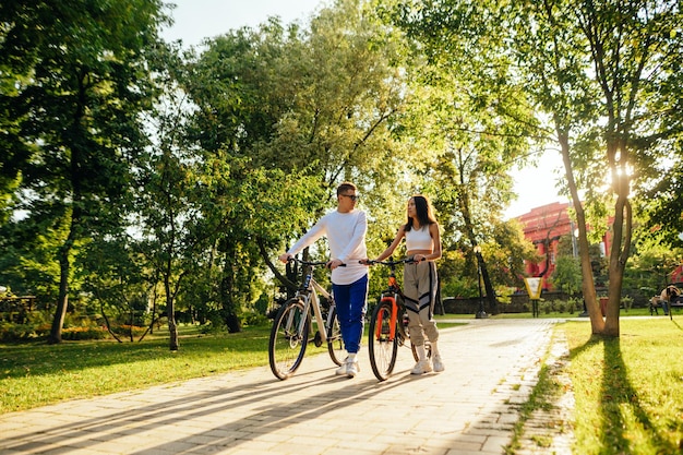 Schönes junges Paar, Mann und Frau, fahren Fahrräder auf der Gasse im Park und kommunizieren