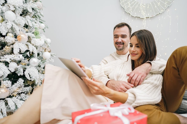 Schönes junges Paar mit digitalem Tablet an Silvester, das zu Hause ausruht