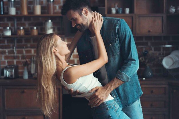 Schönes junges Paar schaut sich an und lächelt beim Tanzen in der Küche.