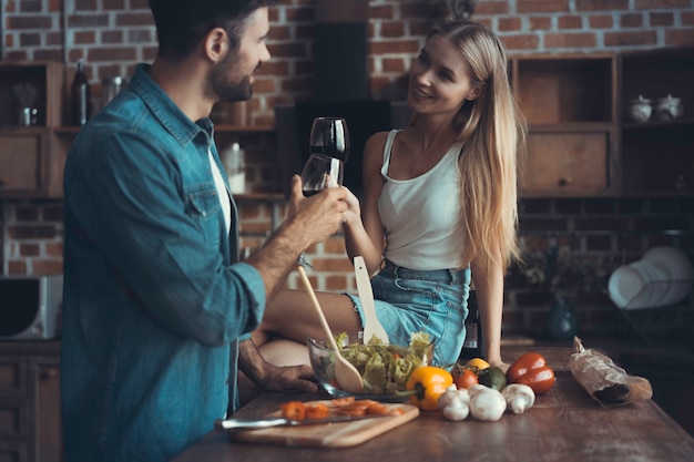 Schönes junges Paar trinkt Wein und lächelt beim Kochen in der Küche zu Hause.