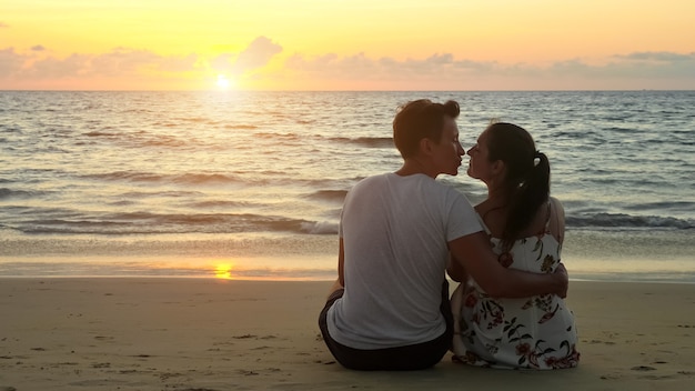 Schönes junges Paar umarmt und küsst am leeren Meeresstrand den Sonnenuntergang im tropischen Resort in abendlicher Rückansicht?