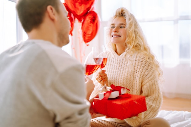 Schönes junges Paar zu Hause, das den Valentinstag feiert Liebhaber beschenken sich gegenseitig