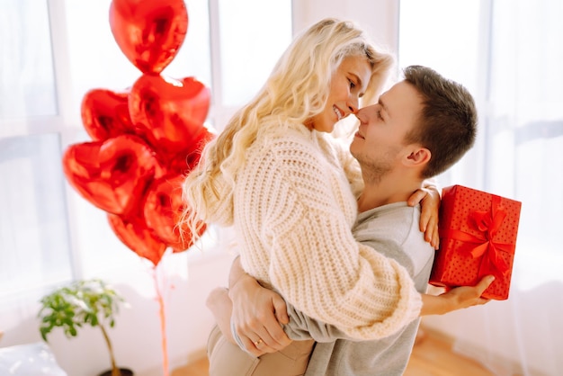 Schönes junges Paar zu Hause, das den Valentinstag feiert Liebhaber beschenken sich gegenseitig