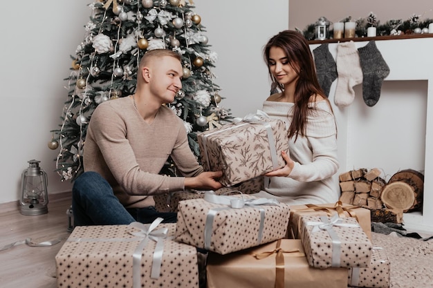 Schönes junges romantisches Paar, das offene Geschenke sitzt, präsentiert mit Girlanden