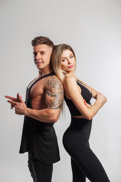 Schönes junges sportliches Paar posiert Rücken an Rücken im Studio. Schönes junges Fitness-Mädchen mit schlankem Körper und gutaussehender, muskulöser, athletischer Mann in schwarzer Sportkleidung