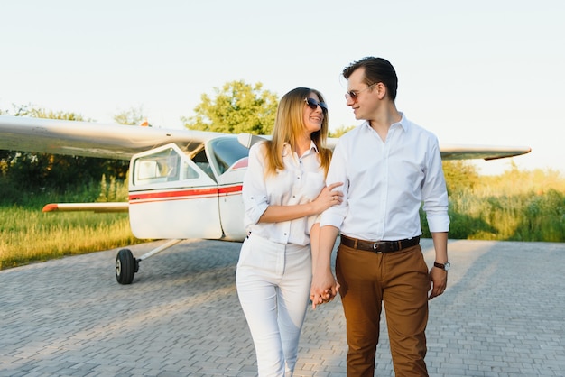 Schönes junges stilvolles Paar in der offiziellen Kleidung, die im Privatflugzeug steht