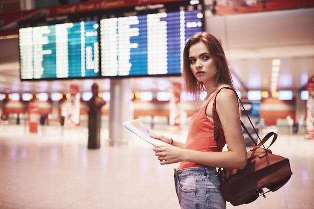 Schönes junges Touristenmädchen mit Rucksack im internationalen Flughafen