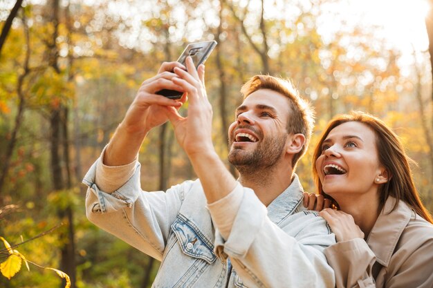 Schönes junges verliebtes Paar mit Handy, während es Zeit im Herbstpark verbringt und ein Selfie macht