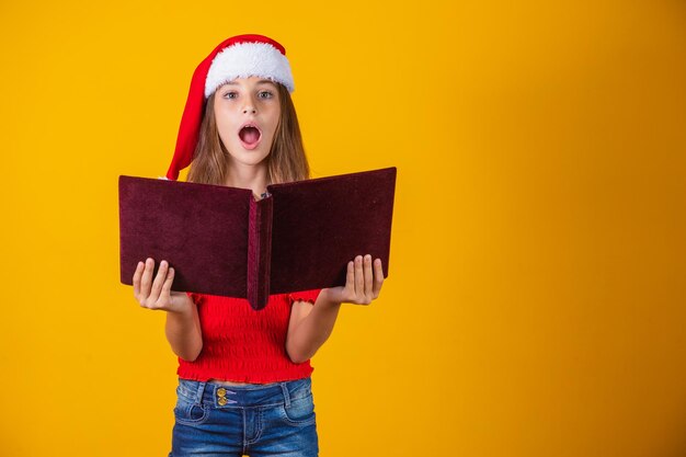 Schönes kaukasisches Kindermädchen mit einem roten samtigen Buch, das Weihnachtsgeschichten liest.