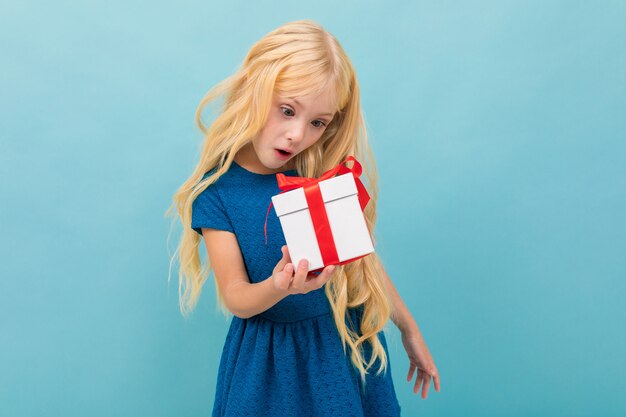 Schönes kaukasisches Mädchen hält einen weißen Kasten mit Geschenk und hat viele Gefühle, die auf Blau lokalisiert werden