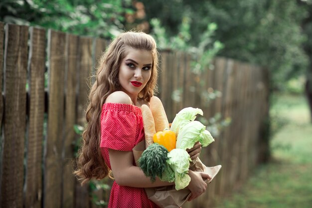Schönes kaukasisches Mädchen im roten Kleid, das eine Tasche des Lebensmittels hält