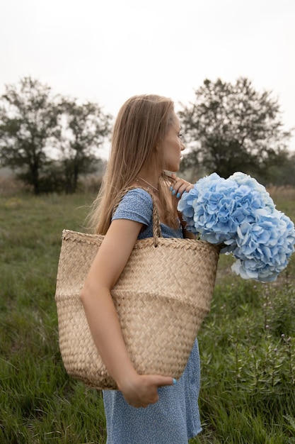 Schönes kaukasisches Mädchen in einem blauen Kleid geht mit einem Blumenkorb durch das Feld