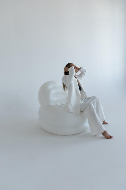 Foto schönes kaukasisches mädchen in einem weißen anzug sitzt in einer modischen pose im studio auf weißem hintergrund