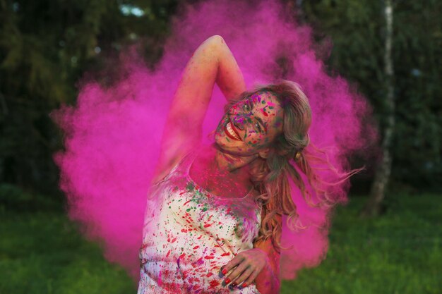 Schönes kaukasisches Modell mit lockigem Haar, das in einer Wolke aus rosa trockener Farbe posiert und das Holi-Festival feiert