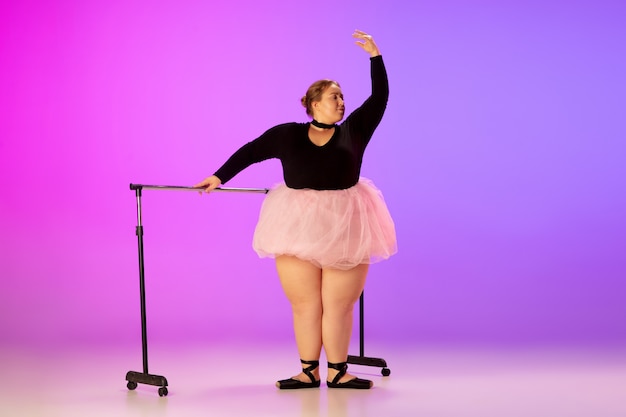 Schönes kaukasisches Plus-Size-Model, das Balletttanz auf einem lilarosafarbenen Studio mit Farbverlauf übt