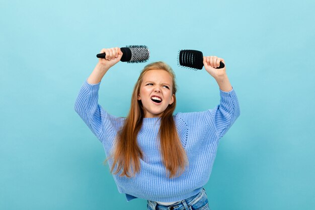 Schönes kaukasisches Teenager-Mädchen mit braunen Haaren im blauen Kapuzenpulli mit Haarkämmen lokalisiert auf Blau