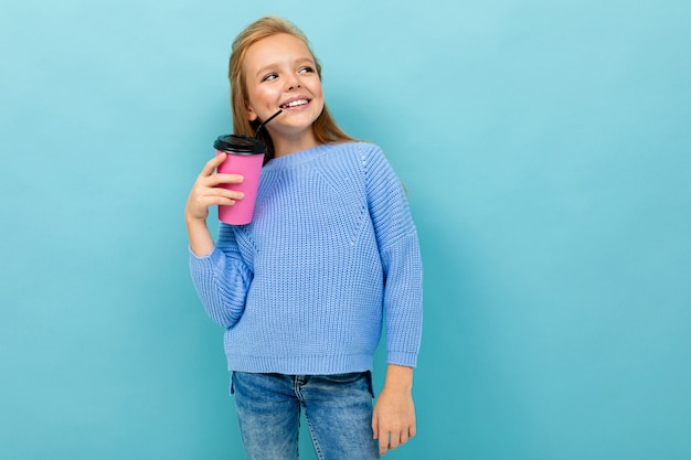Schönes kaukasisches Teenager-Mädchen mit braunen Haaren im blauen Kapuzenpulli trinkt Kaffee mit rosa Tasse lokalisiert auf blauem Hintergrund