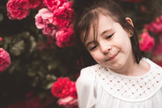 Schönes Kind, das draußen mit rosa Rosen posiert