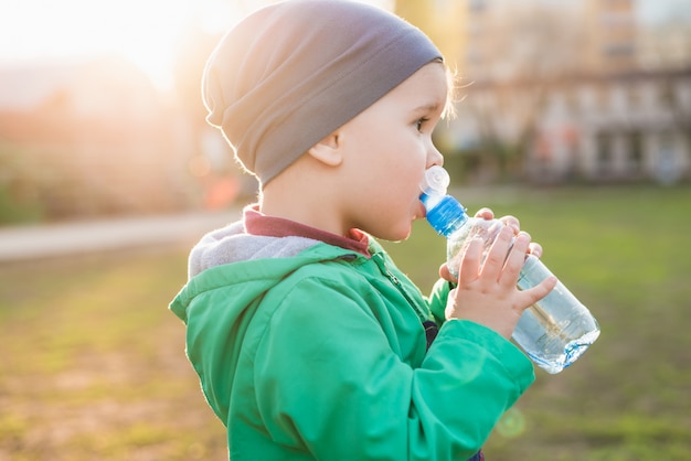 Schönes Kind trinkt Wasser von einer Flasche an einem heißen Sommertag