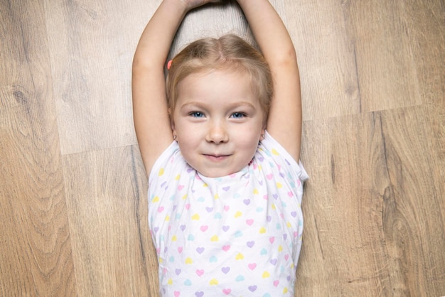 Schönes Kindermädchen hob ihre Hände hoch und lag auf einem Holzboden Draufsicht flach lag