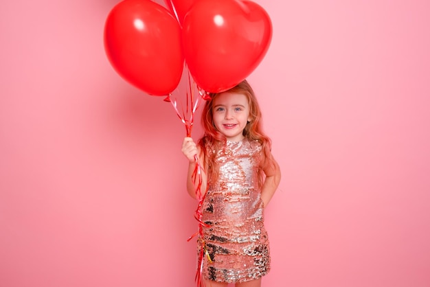 Schönes Kindermädchen im Kleid mit Pailletten mit romantischen roten Herzballons auf rosa Hintergrund