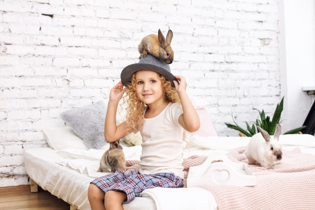 Schönes Kindermädchen mit lockigem Haar und flauschigen Kaninchentieren, die auf einem Hut sitzen