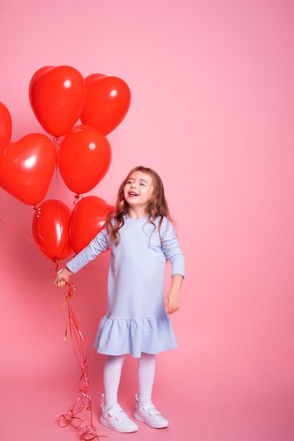 Schönes Kindermädchen mit romantischen Luftballons des roten Herzens auf rosa Hintergrundkonzept des Valentinstags