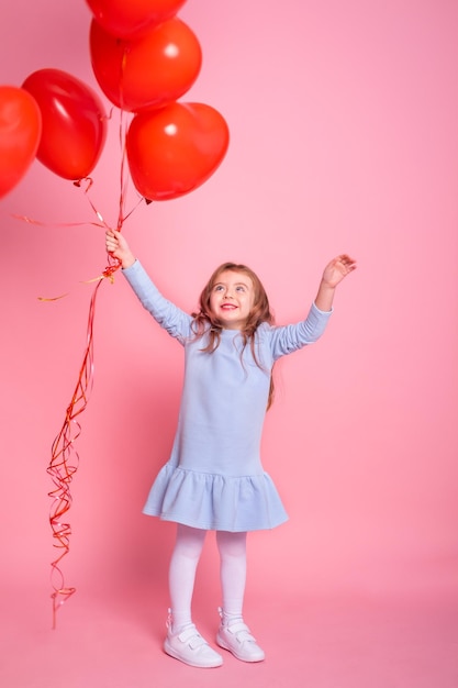 Schönes Kindermädchen mit romantischen Luftballons des roten Herzens auf rosa Hintergrundkonzept des Valentinstags