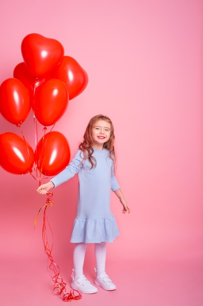 Schönes Kindermädchen mit romantischen Luftballons des roten Herzens auf rosa Hintergrundkonzept des Valentinstags