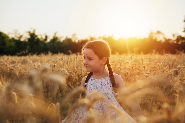 Schönes Kindermädchen mit Zöpfen in einem Kleid auf dem Weizengebiet