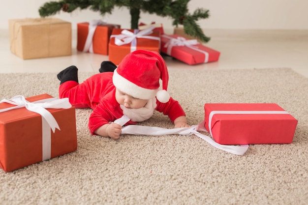 Schönes kleines Baby feiert Weihnachten. Neujahrsfeiertage. Baby in einem Weihnachtskostüm und in Weihnachtsmütze und Geschenkbox.