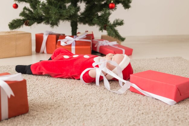 Schönes kleines Baby feiert Weihnachten. Neujahrsfeiertage. Baby in einem Weihnachtskostüm und in Weihnachtsmütze und Geschenkbox.