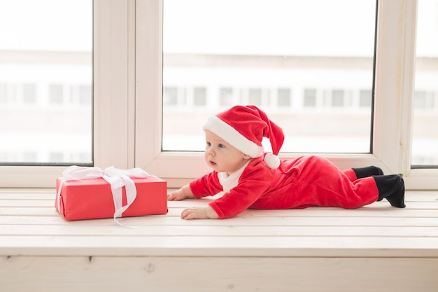 Schönes kleines Baby feiert Weihnachten. Neujahrsfeiertage. Baby in einem Weihnachtskostüm und in Weihnachtsmütze.