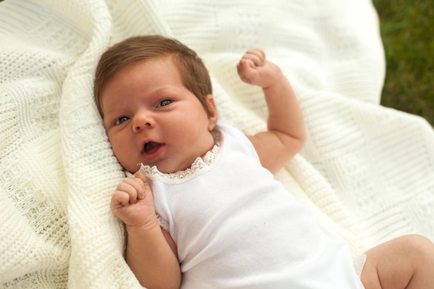 Schönes kleines Baby in weißer Kleidung auf der weißen Decke im Gras