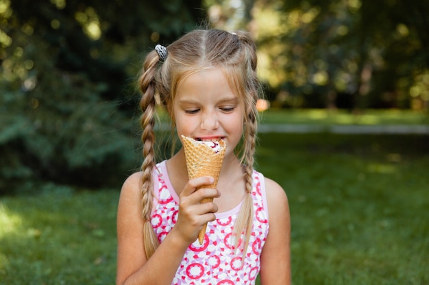 Schönes kleines blondes Mädchen, das im Sommer im Park Eis isst. fröhliches Mädchen mit Eis.