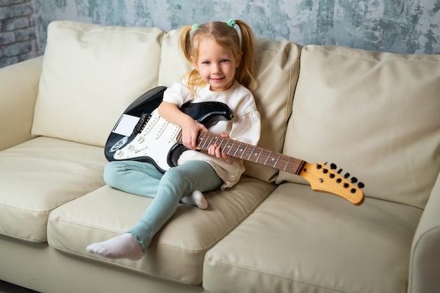 schönes kleines Mädchen auf der Couch mit einer E-Gitarre