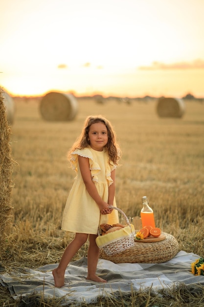 Schönes kleines Mädchen auf einem Picknick auf einem Feld in der Nähe eines trockenen Heuporträts bei sonnigem Sonnenuntergang