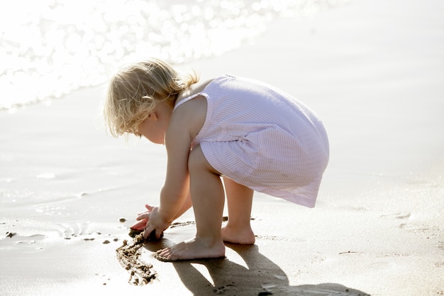 Schönes kleines Mädchen, das auf dem Strand spielt