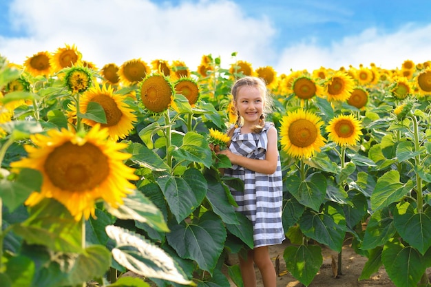 Schönes kleines Mädchen, das die Natur genießt Fröhliches lächelndes weibliches Kind, das auf dem Sonnenblumenfeld steht