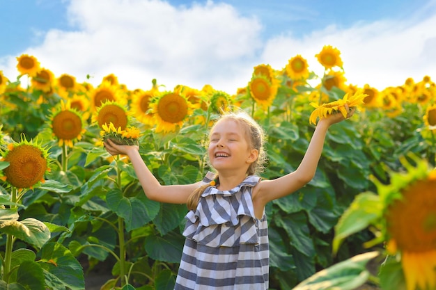 Schönes kleines Mädchen, das die Natur genießt Fröhliches lächelndes weibliches Kind, das auf dem Sonnenblumenfeld steht