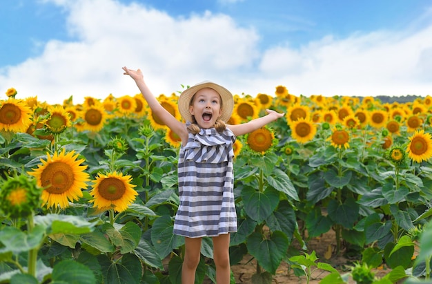 Schönes kleines Mädchen, das die Natur genießt Fröhliches lächelndes weibliches Kind, das auf dem Sonnenblumenfeld steht