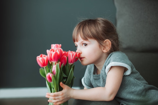 Schönes kleines Mädchen, das eine Blume der rosa Tulpe in einer Vase schnüffelt