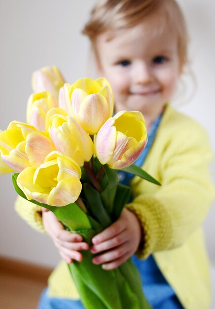 Schönes kleines Mädchen, das einen Blumenstrauß von gelben Tulpen hält