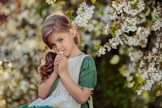 Schönes kleines Mädchen, das in einem blühenden Garten sitzt